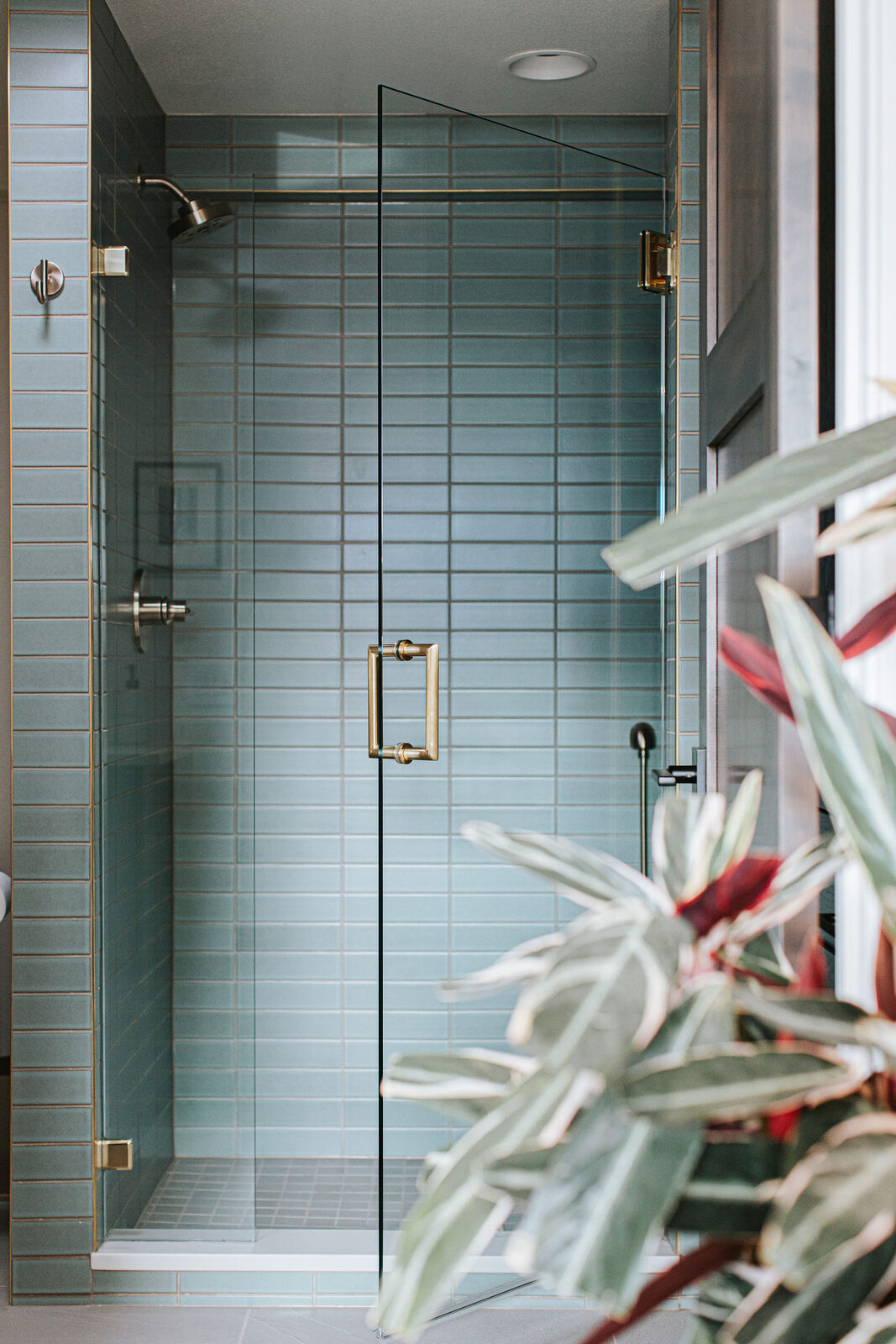 Blue tiled shower with glass enclosure and brass hardware